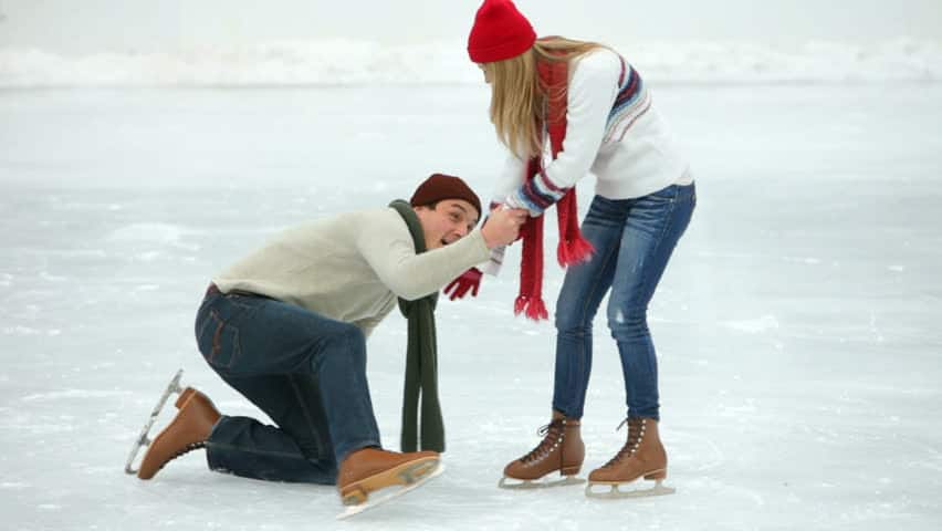 young woman helping boyfriend get up after falling while ice skating