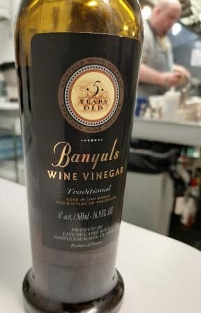 a bottle of Banyul vinegar with chef cooking in the background