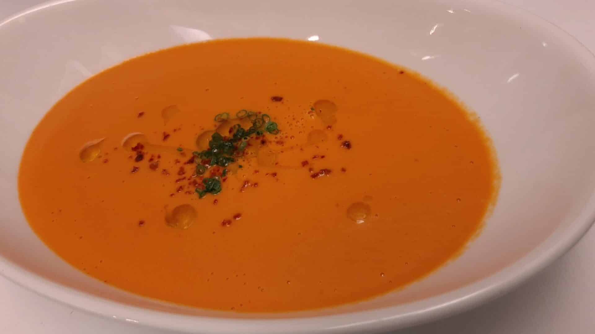 a white bowl filled with Tomato bisque soup sprinkled with sliced chives and drizzled with olive oil|heirloom tomatoes piled high|Best tomato bisque soup recipe|tomatoes of various shapes