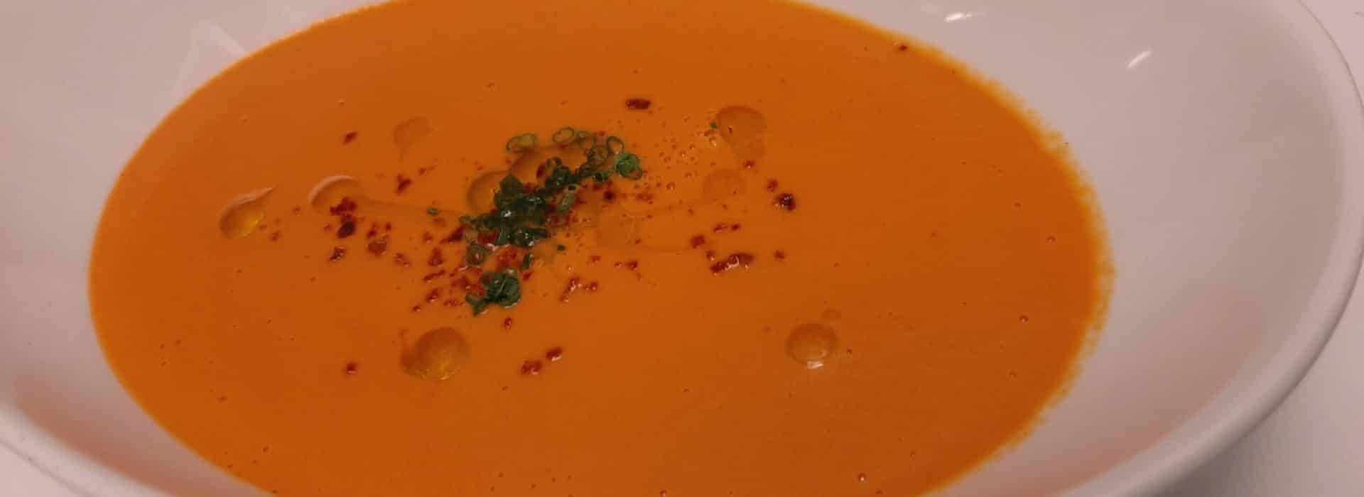a white bowl filled with Tomato bisque soup sprinkled with sliced chives and drizzled with olive oil|heirloom tomatoes piled high|Best tomato bisque soup recipe|tomatoes of various shapes