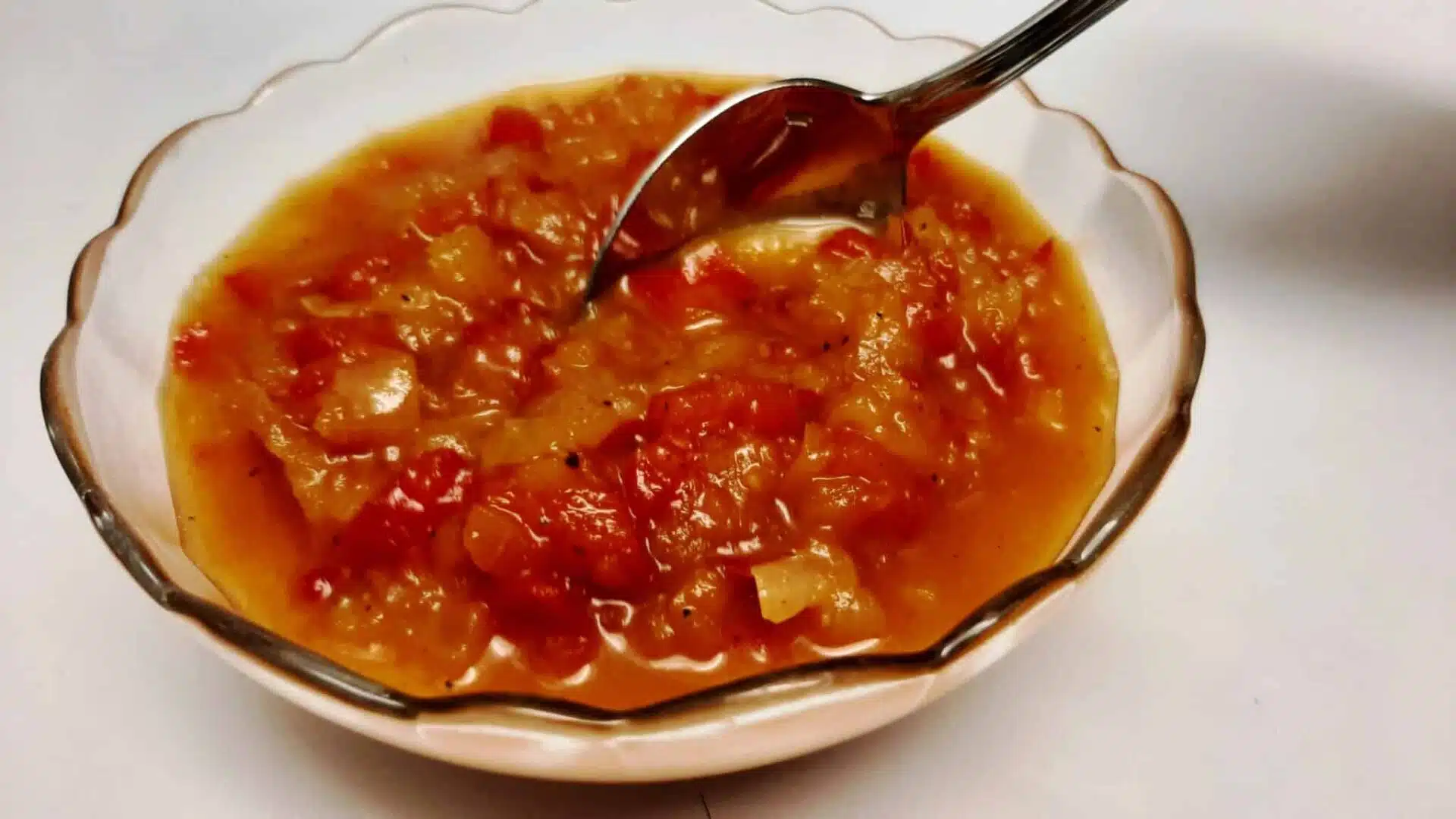 a glass bowl of sweet pepper relish with a spoon resting on the side|chef spooning pepper relish into a glass bowl