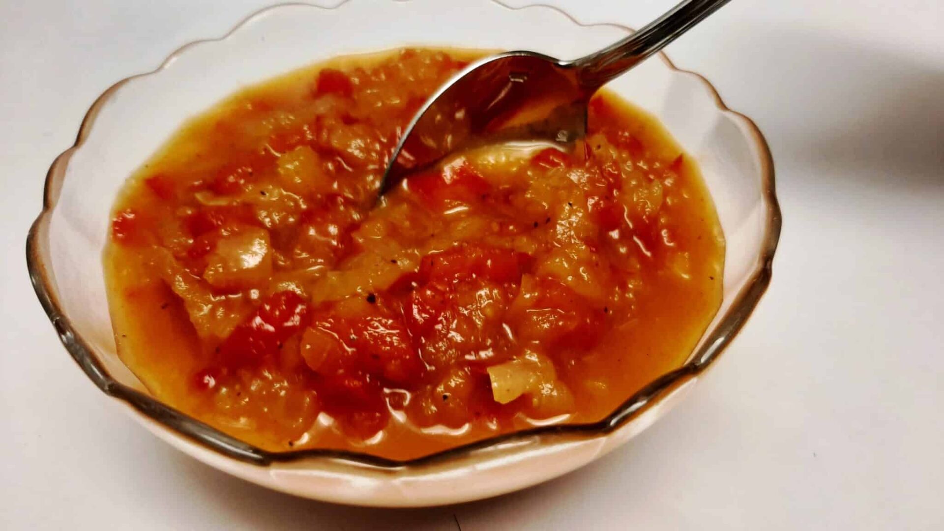 a glass bowl of sweet pepper relish with a spoon resting on the side|chef spooning pepper relish into a glass bowl