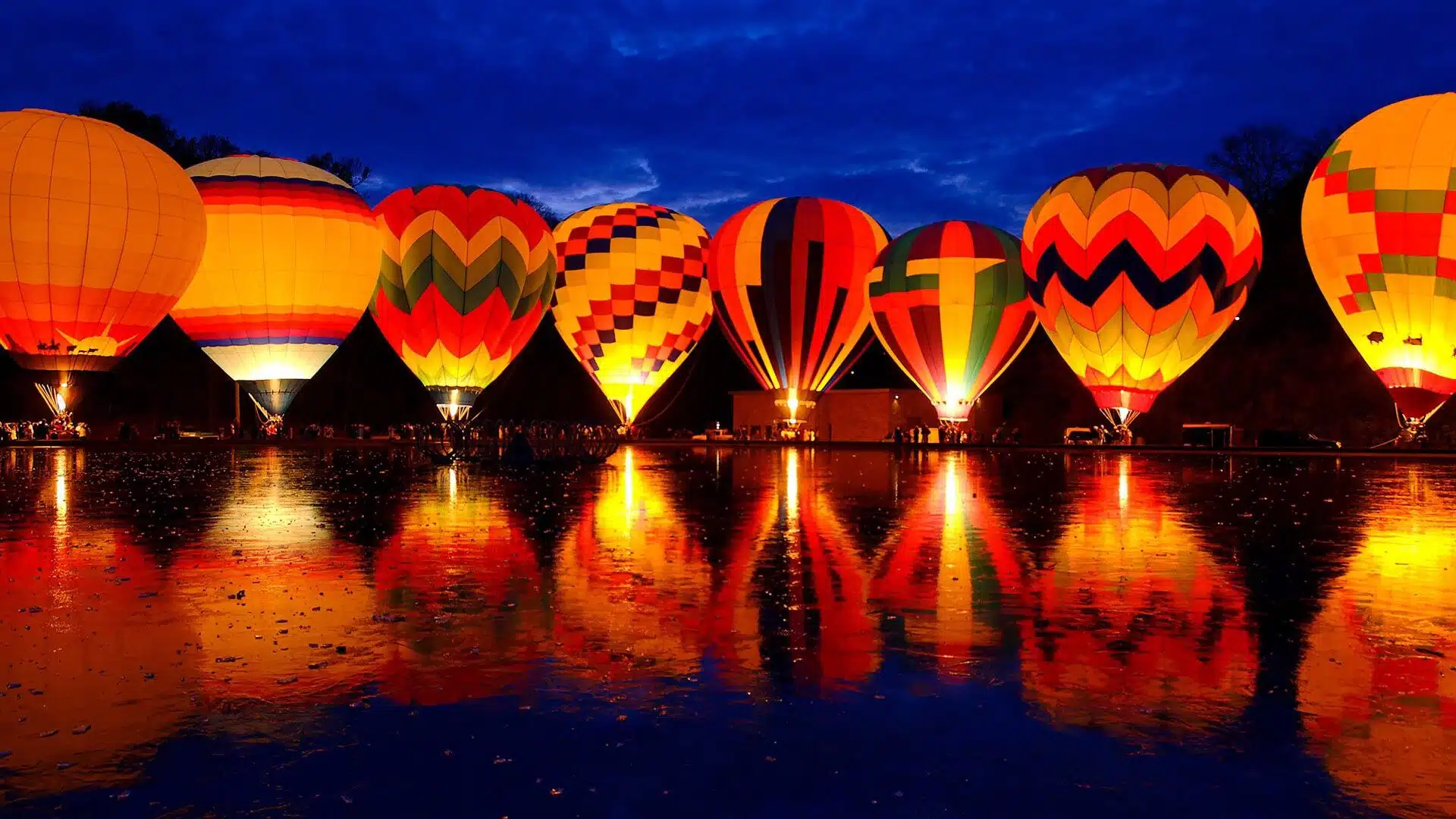 night scene of illuminated colorful balloons along a lake in Quechee vermont|several colorful balloons floating against a blue sky