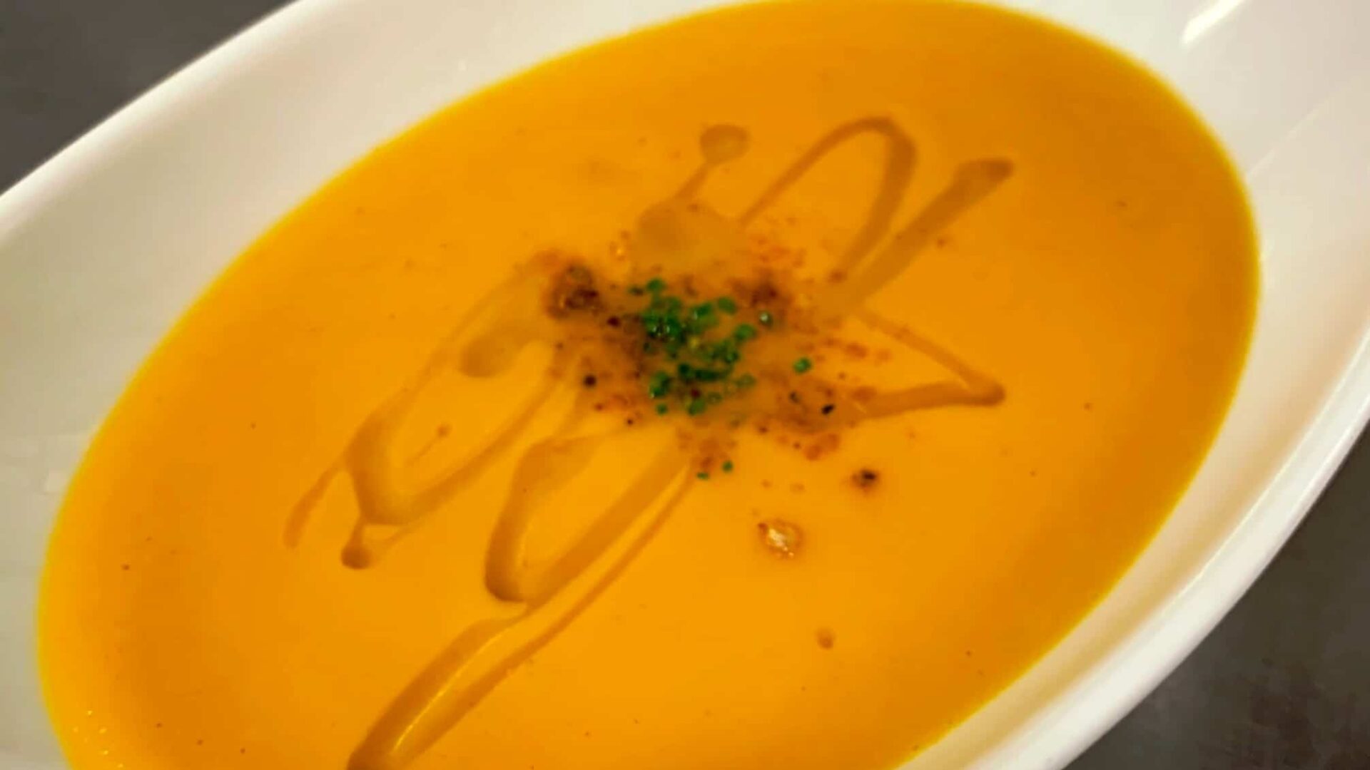 An oval white bowl filled with sweet potato soup|A bowl of sweet potato coconut curry soup|Chef spooning pepper relish into a glass bowl