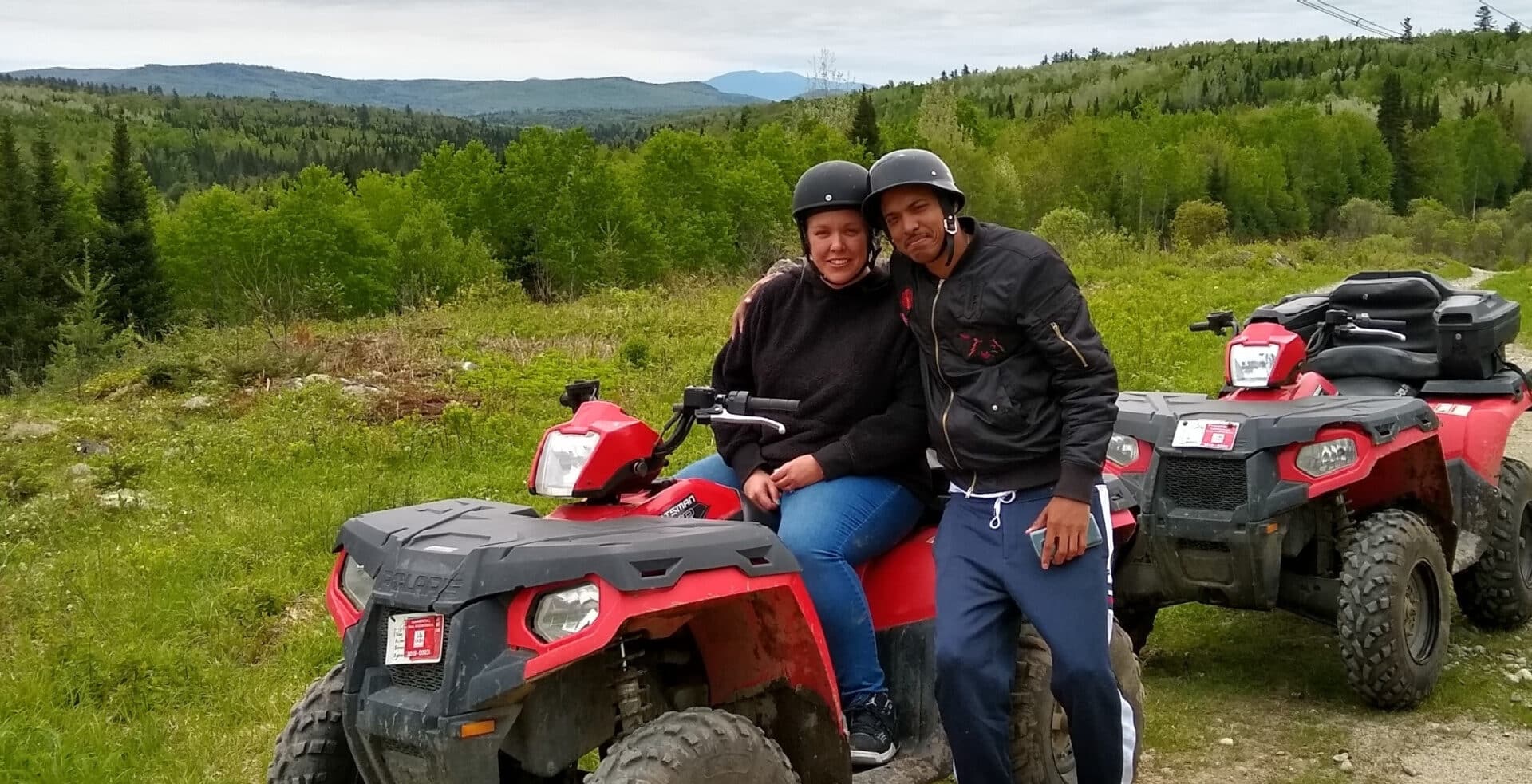 young couple sitting on ATV with mountains behind them