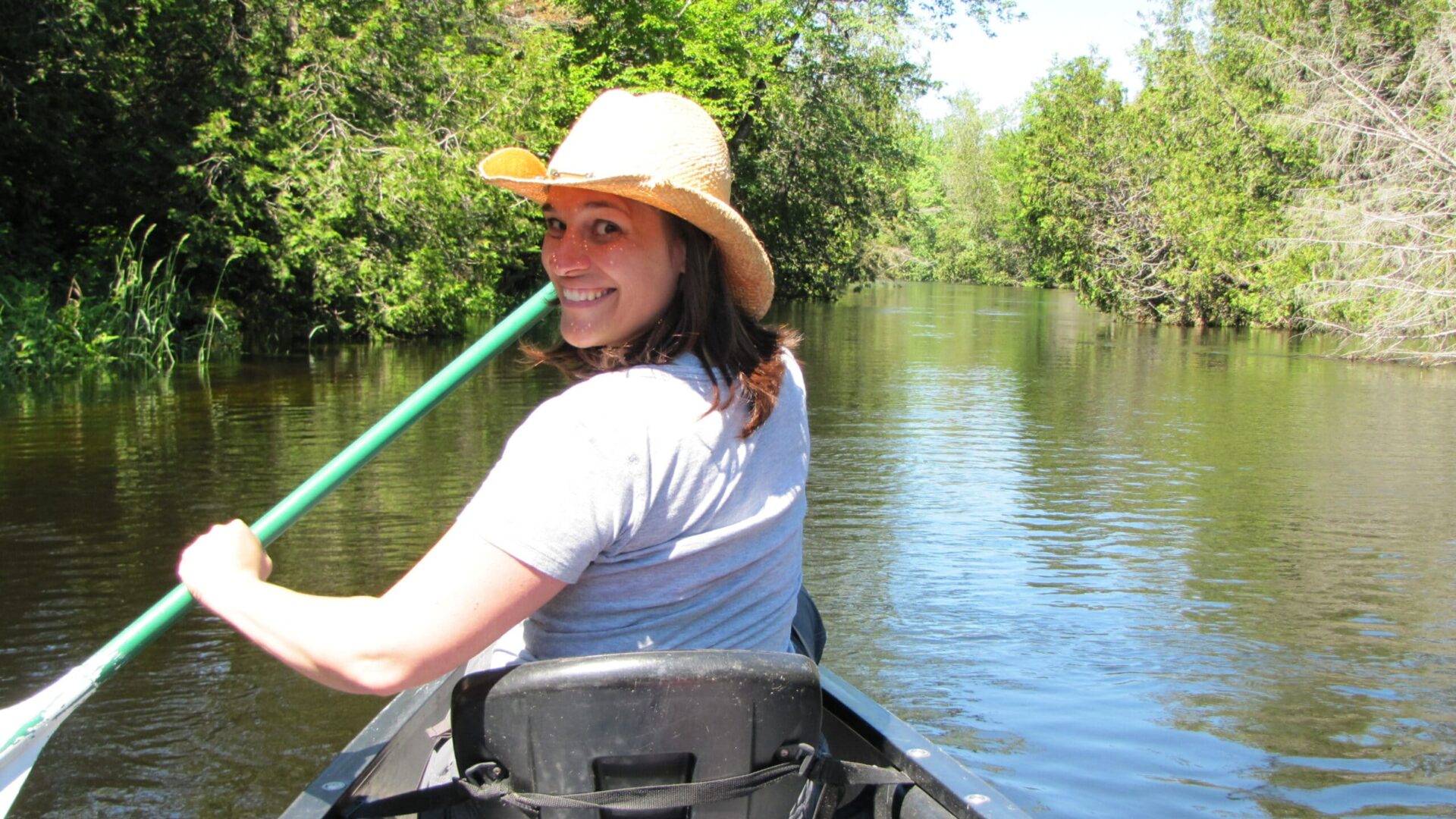 smiling young gal paddling a canoe on a serene river