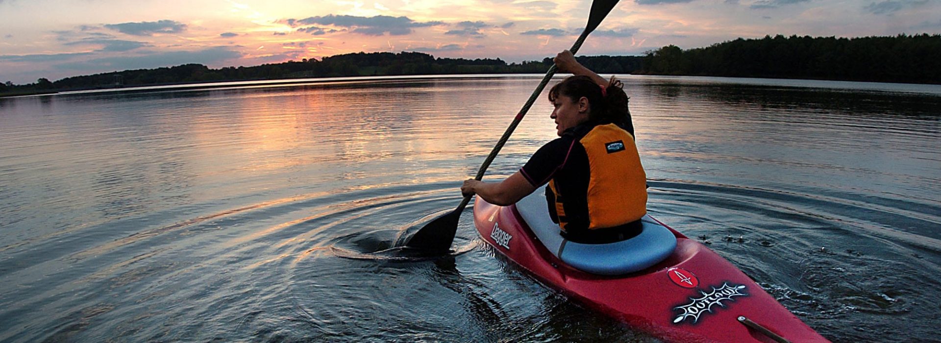 girl paddling a kayak on the river at sunset