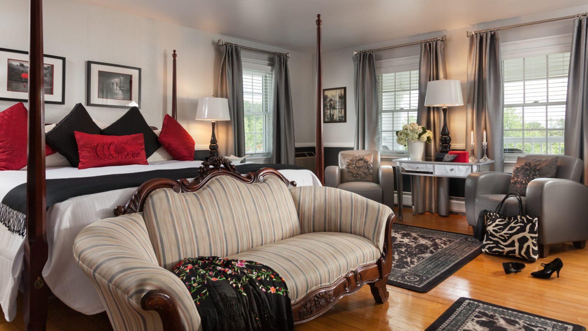 empire sofa in front of a pencil post bed near two leather chairs and a mirror covered table