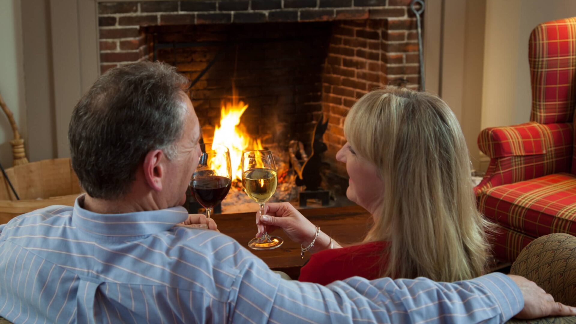 Couple toasting each other with wine in front of a fireplace|discount winter travel deals