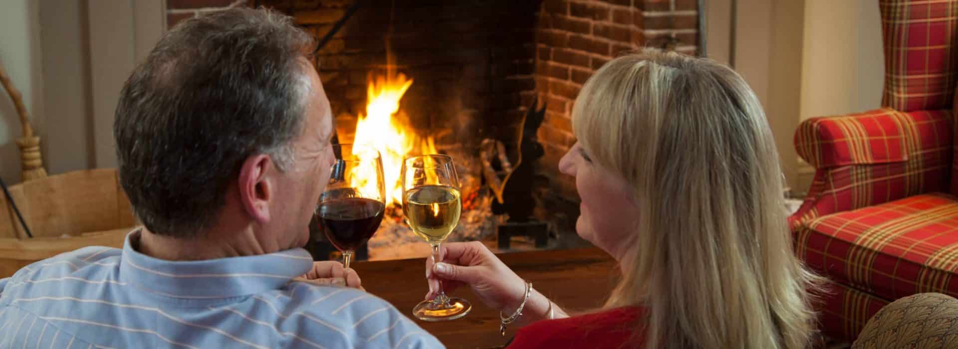 Couple toasting each other with wine in front of a fireplace|cyber monday getaway deals