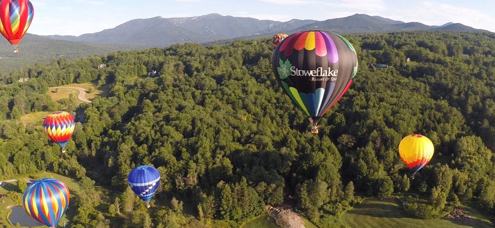 several colorful balloons in the air at the Stoweflake Hot Air Balloon Festival Stowe Vermont|several colorful hot air balloons rising off the ground