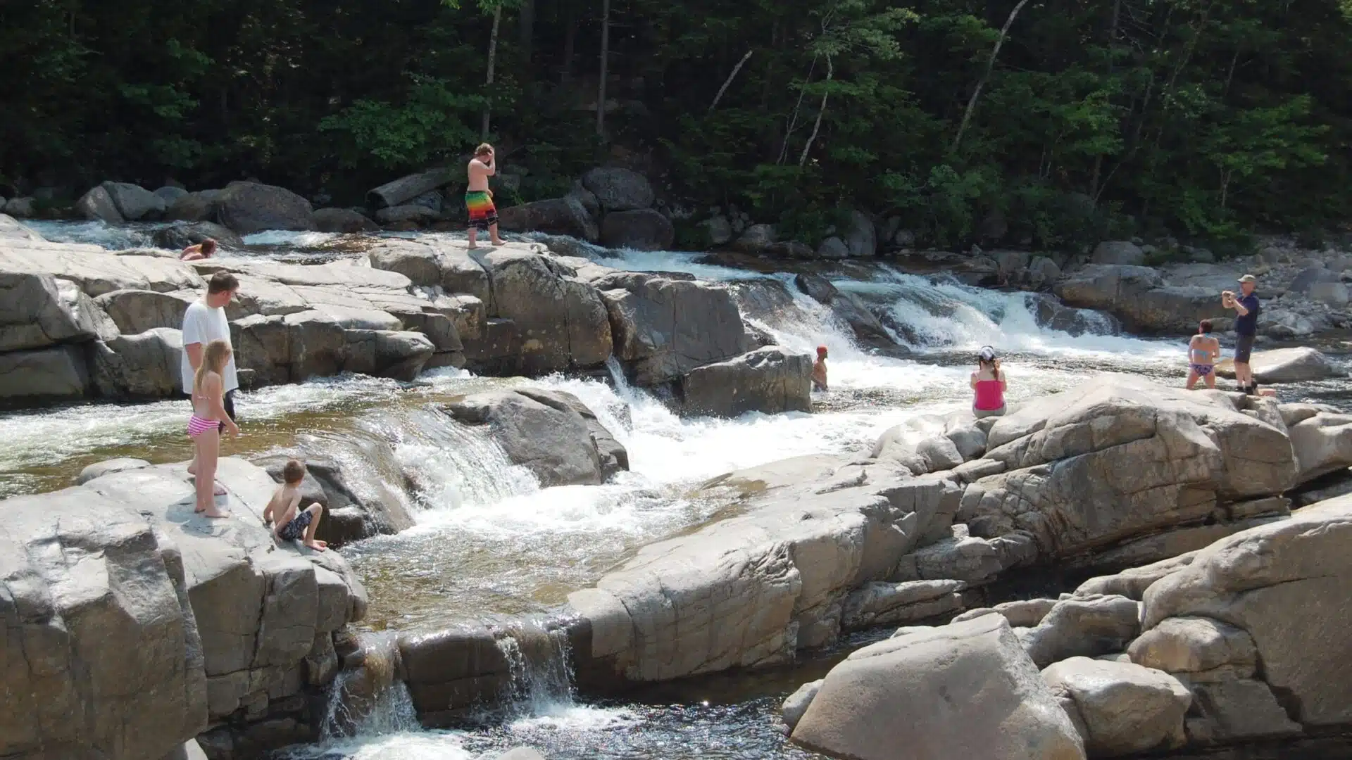 people on the rocks at a Swimming Holes in the White Mountains New Hampshire|rushing water at the swimming holes in Vermont and White Mountains New Hampshire|people enjoying the Swimming holes waterfalls in Franconia New Hampshire