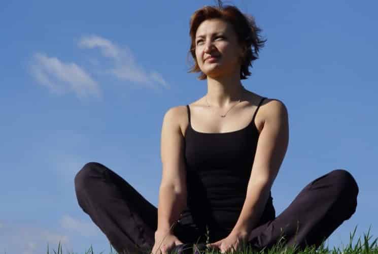 Close up view of woman dressed in black workout clothes sitting on green grass doing a yoga pose