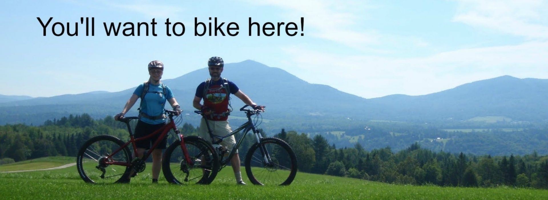 two people standing next to their mountain bikes on a grassy hill.