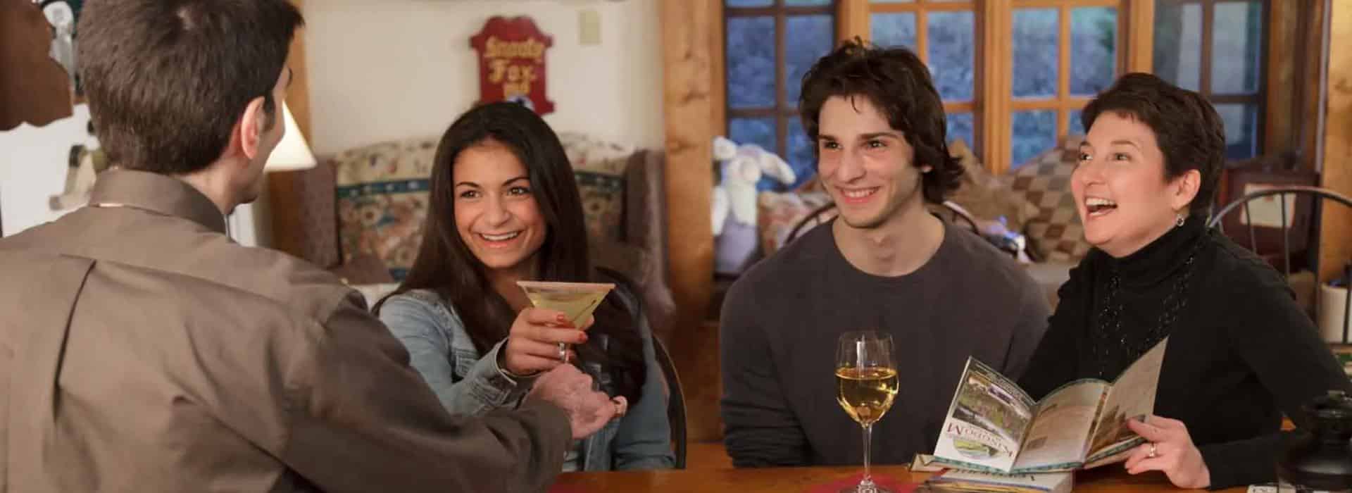People sitting at a wooden bar smiling, drinking, and talking to bartender