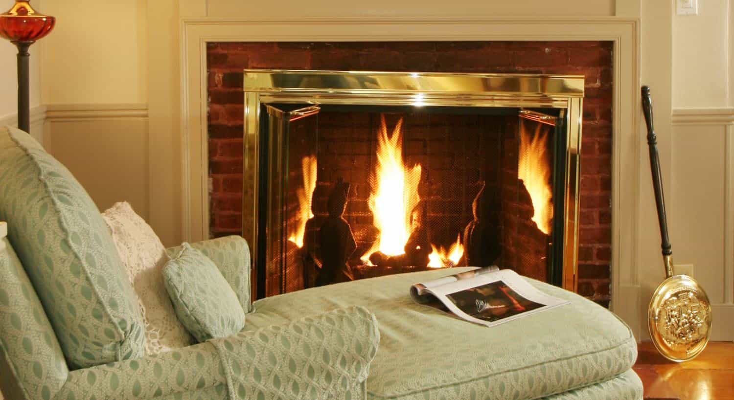 Light green upholstered chaise near lighted fireplace