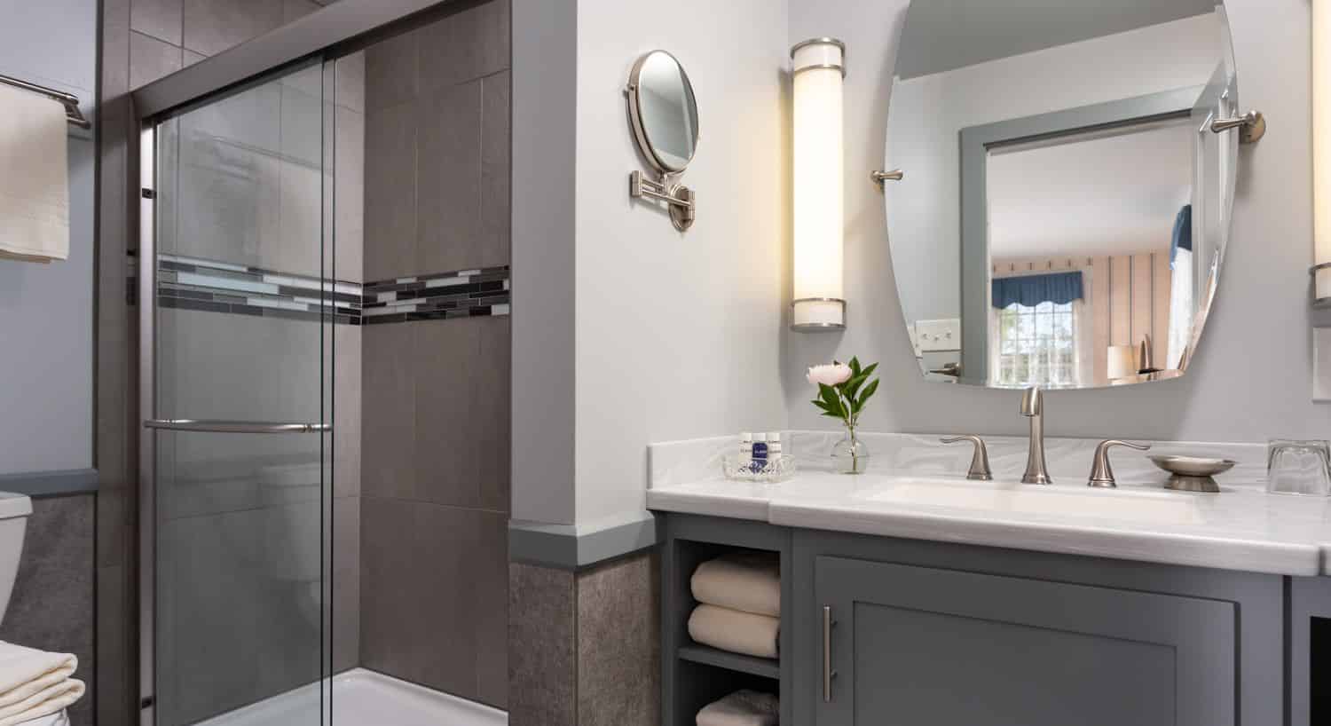 Bathroom with light gray walls, dark gray vanity, gray-tiled stand up shower, and large mirror