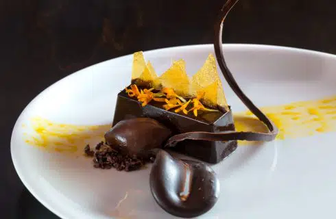 Close up view of a fancy chocolate dish decorated with yellow flowers and yellow sugar triangle pieces on a white porcelain plate