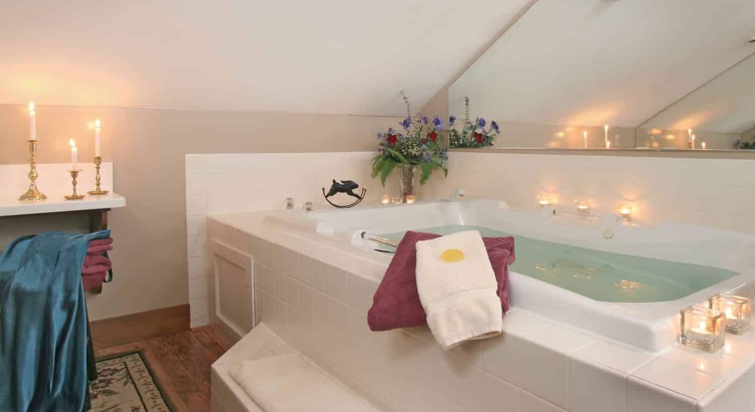 Large whirlpool tub surrounded by white tiles, light cream walls, and lighted candles