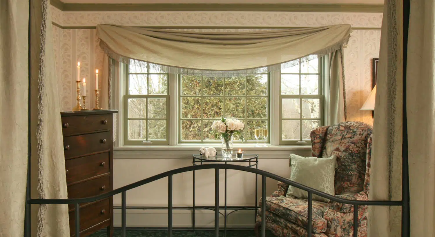 Sitting area with upholstered arm chair, wrought iron and glass table, dark wooden dresser, and view to the outside