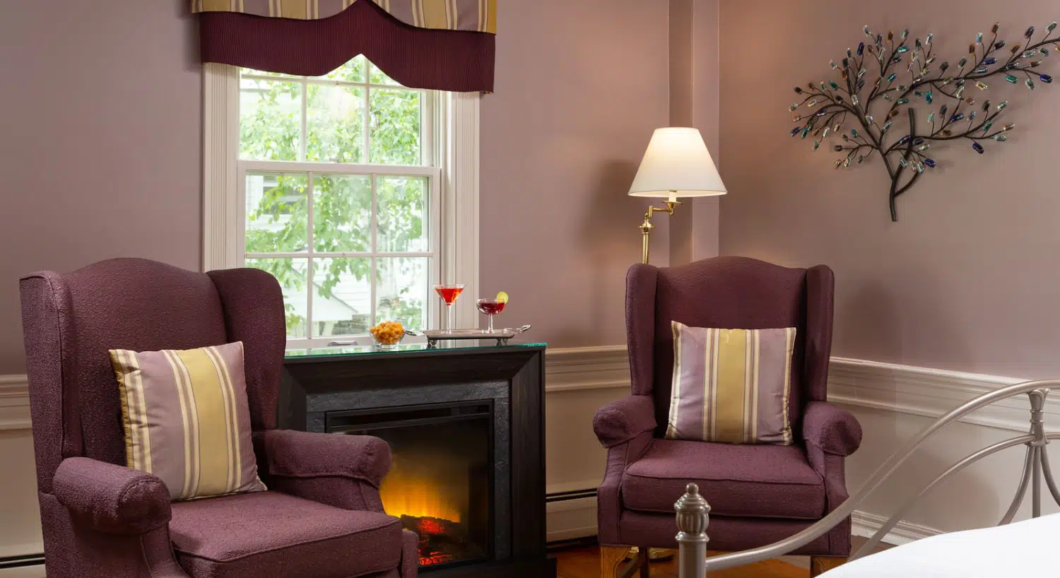 Sitting area in bedroom with light-lavendar walls and white chair rail, purple upholstered arm chairs, and fireplace
