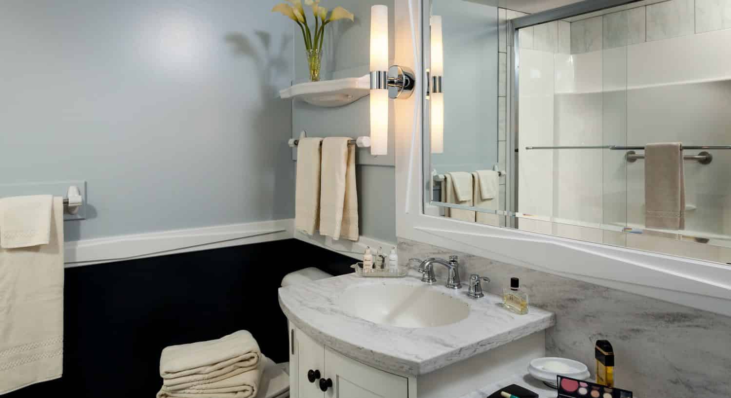 Bathroom with light gray walls on top and black on the bottom under chair rail, white vanity, marble sink, and large white-framed mirror