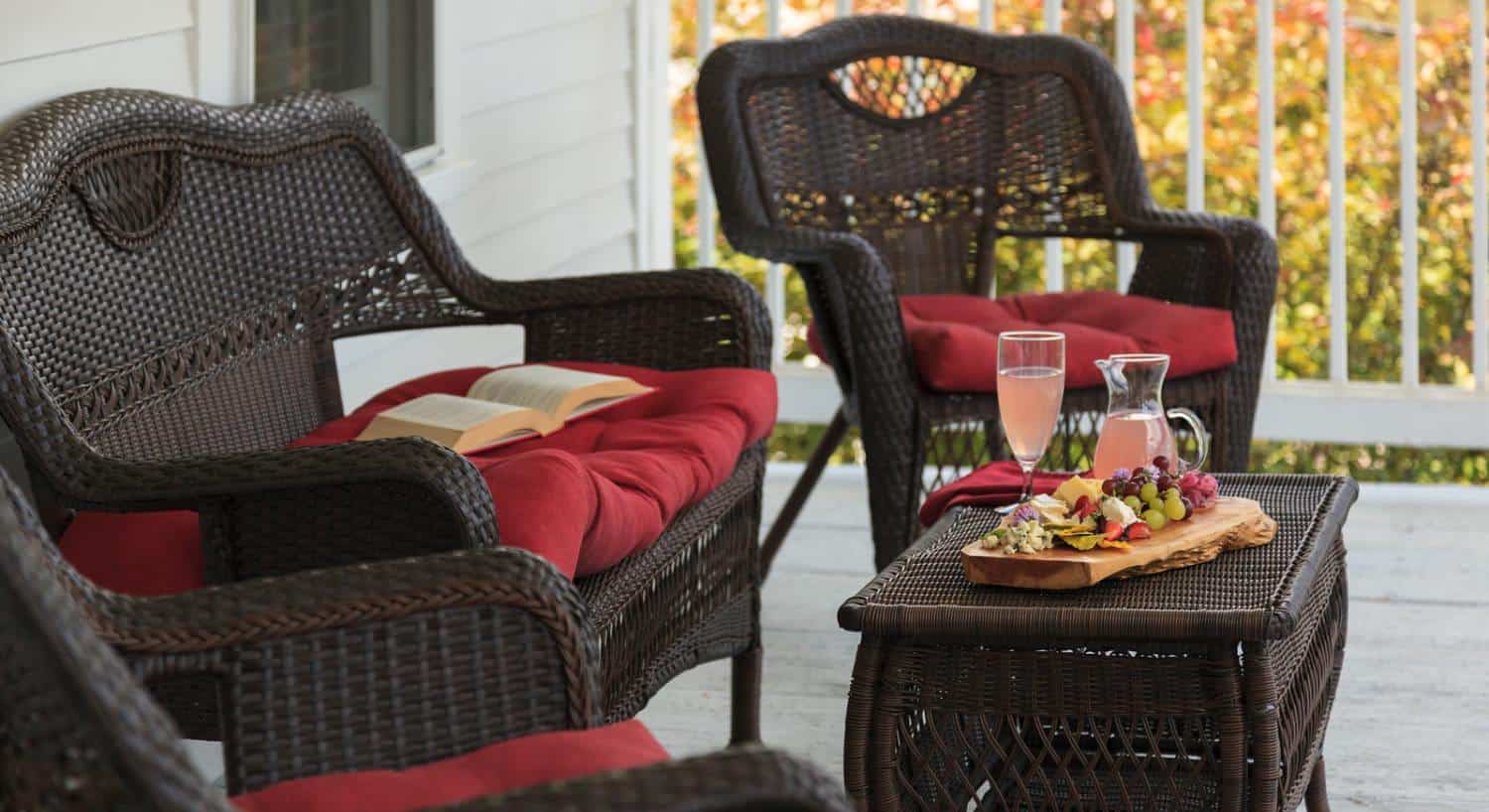 Close up view of dark brown wicker patio furniture on front porch with a glass filled with pink lemonade and tray with fruit and cheese