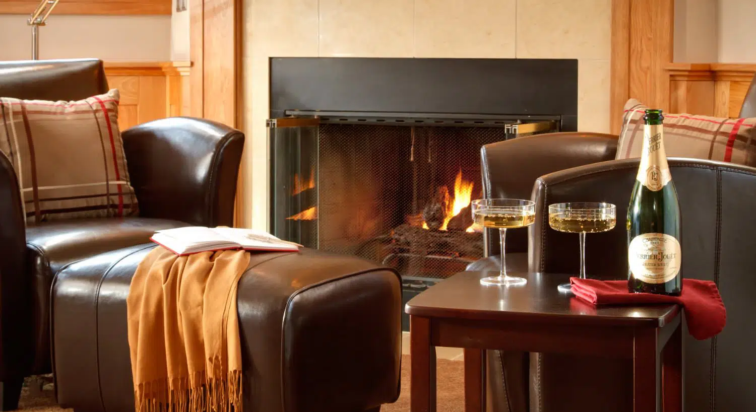 Close up view of sitting area with dark brown leather chairs, wooden end table, glasses full of wine, and a fireplace