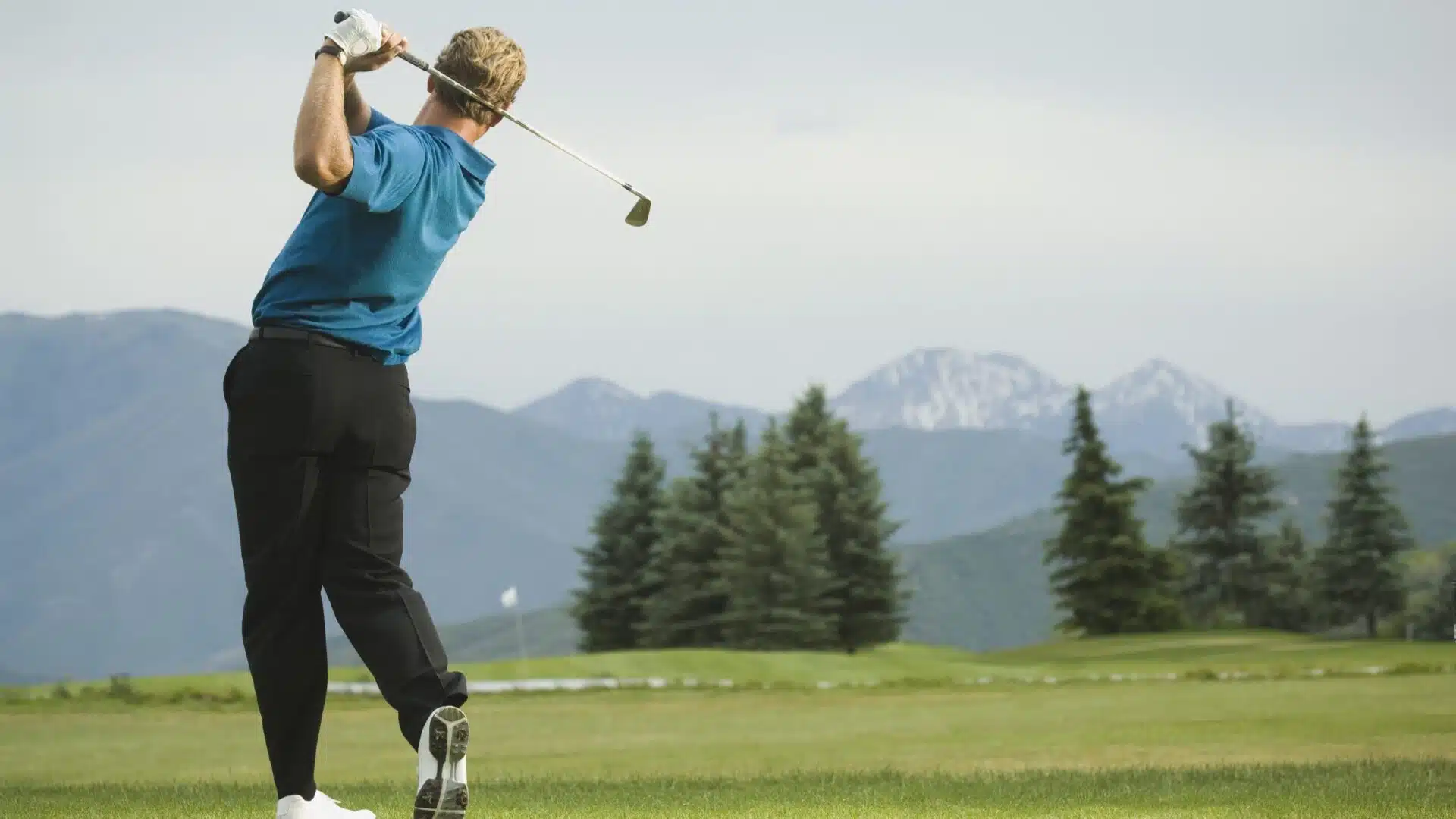 A man swinging a golf club with a backdrop of beautiful mountains