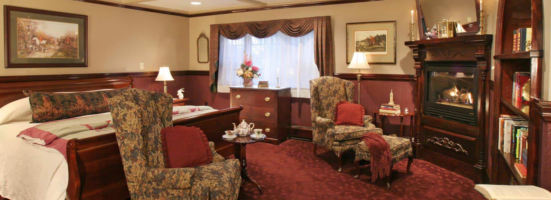 Large bedroom suite with dark wooden sleigh bed, white bedding, burgundy carpeting, sitting area, and fireplace