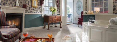 Large bedroom suite with light-colored carpet, floral wallpaper, blue-gray paneled chair rail, whirlpool tub, sitting area, and fireplace