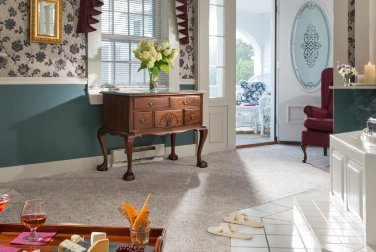 Large bedroom suite with light-colored carpet, floral wallpaper, blue-gray paneled chair rail, whirlpool tub, sitting area, and fireplace