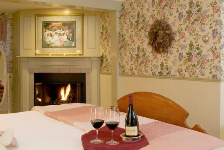 Bedroom with floral wallpaper, light-colored wall below chair rail, wooden bed with white bedding, and fireplace