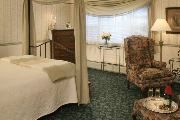 Large bedroom suite with wrought iron canopy bed, white bedding, dark green floral carpeting, sitting area, and fireplace