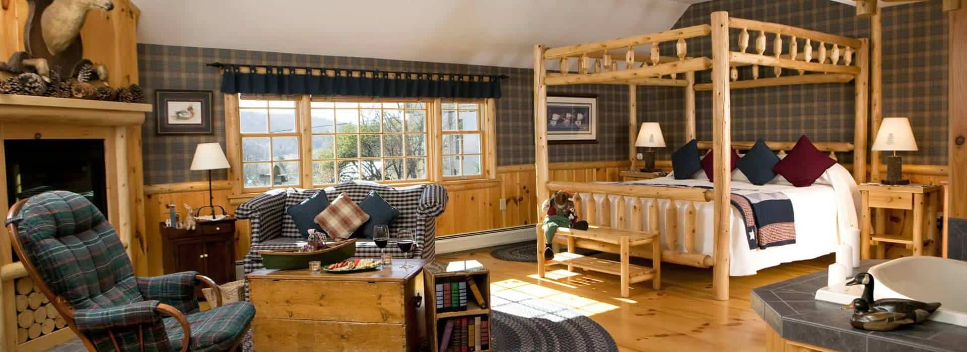 A large bedroom with a rocking chair next to a dark wooden writing desk with chair, situated between two windows in a corner. Canopy bed with lace faux canopy atop tapered posts.