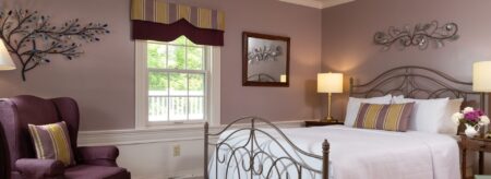 Bedroom with light-lavendar walls and white chair rail, silver wrought iron bed, white bedding, and purple upholstered arm chair