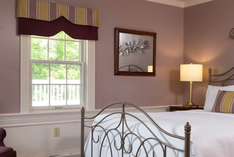 Bedroom with light-lavendar walls and white chair rail, silver wrought iron bed, white bedding, and purple upholstered arm chair