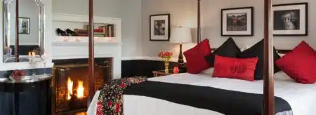 Bedroom with light-gray walls on top and black on bottom of chair rail, dark wooden four-poster bed, white bedding, black and red pillows, and a fireplace