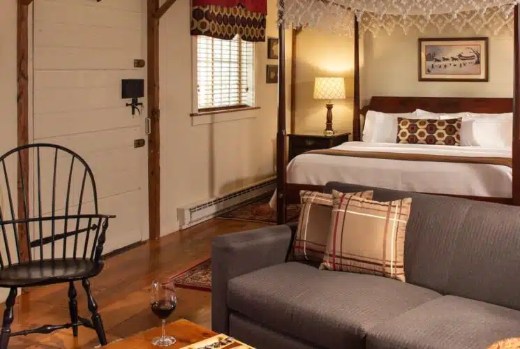 Large bedroom suite with hardwood floors, cream walls, dark wooden four-poster bed, white bedding, and sitting area