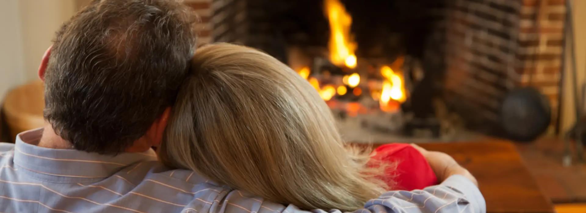 Close up view of the back of a man's and woman's heads as they cuddle next to a burning fireplace