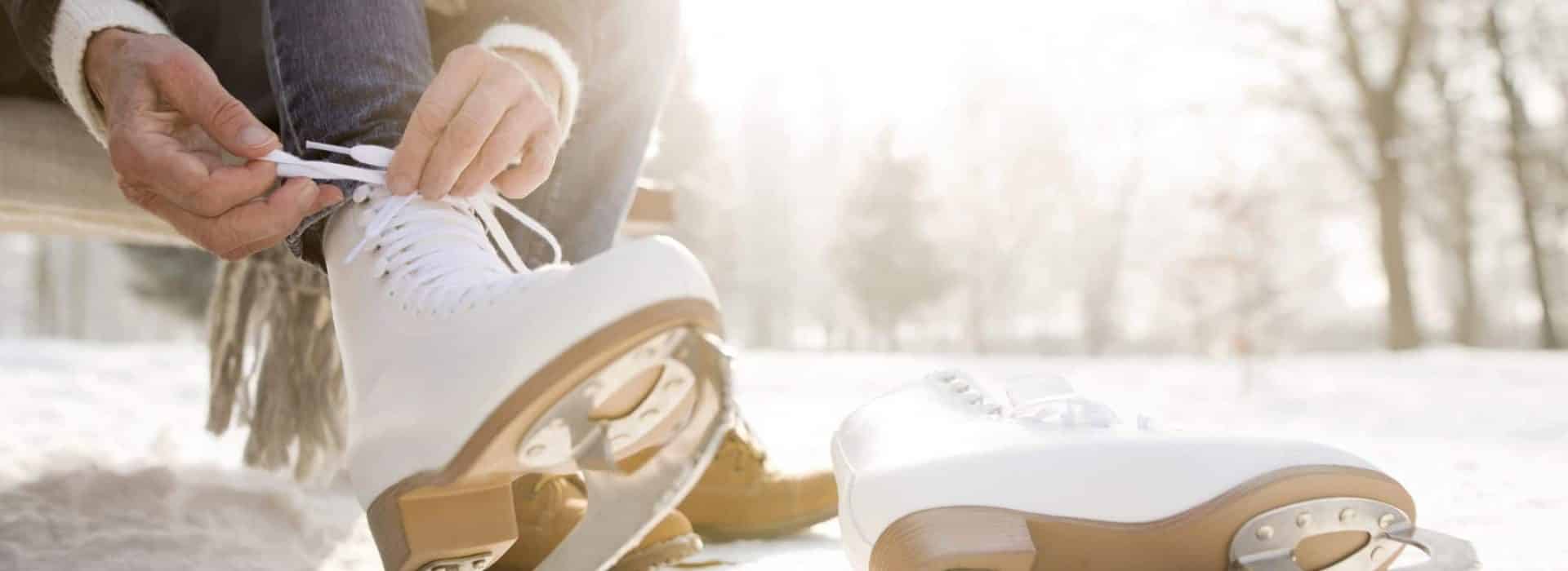 woman tying her white ice skates|young woman helping boyfriend get up after falling while ice skating