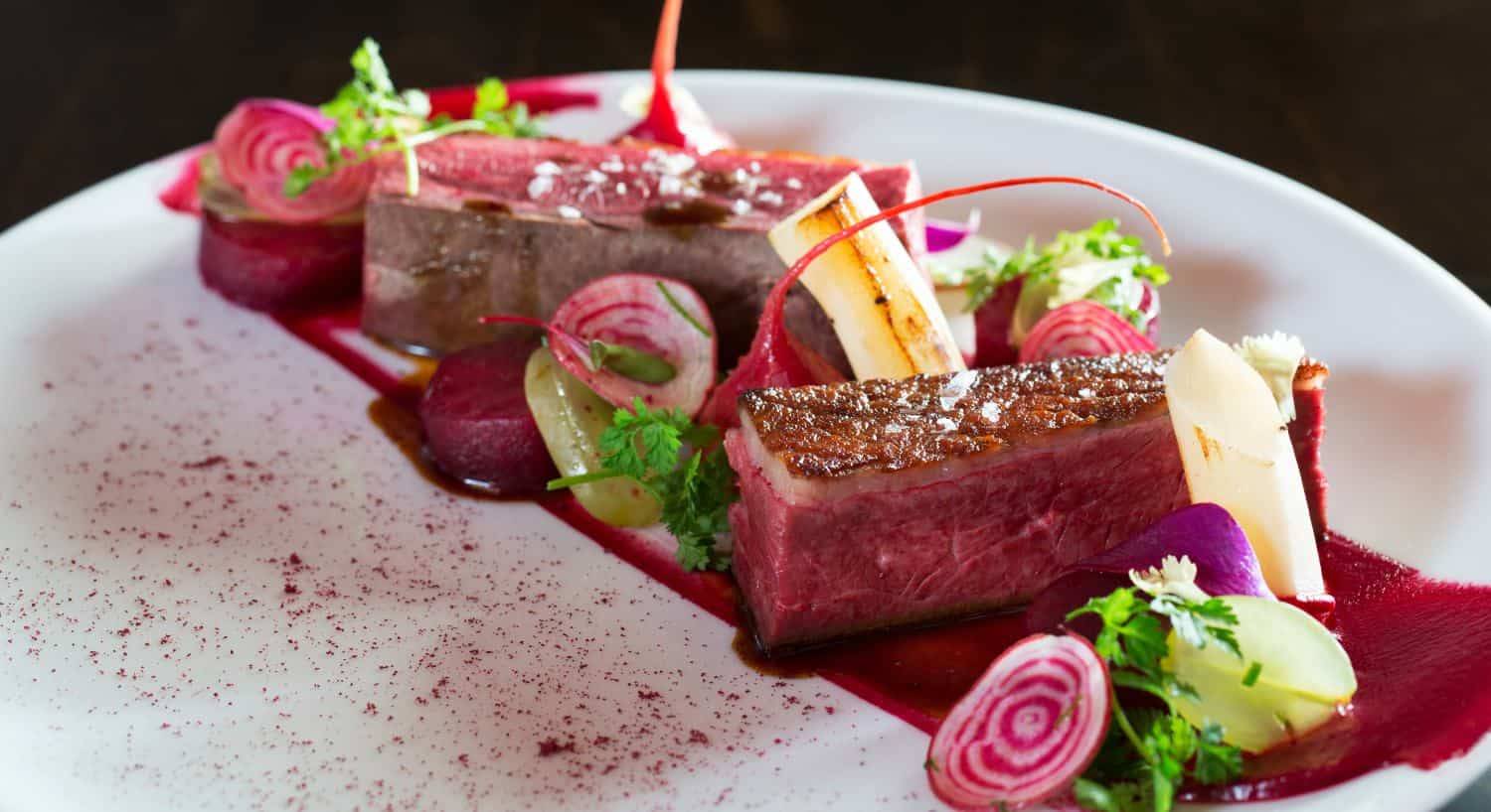 Close up view of a duck dish decorated with beets, radishes, and cilantro on a white porcelain plate