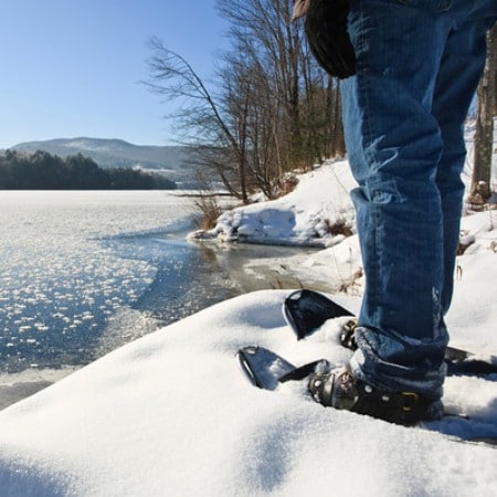 man standing in snowshoes by a river