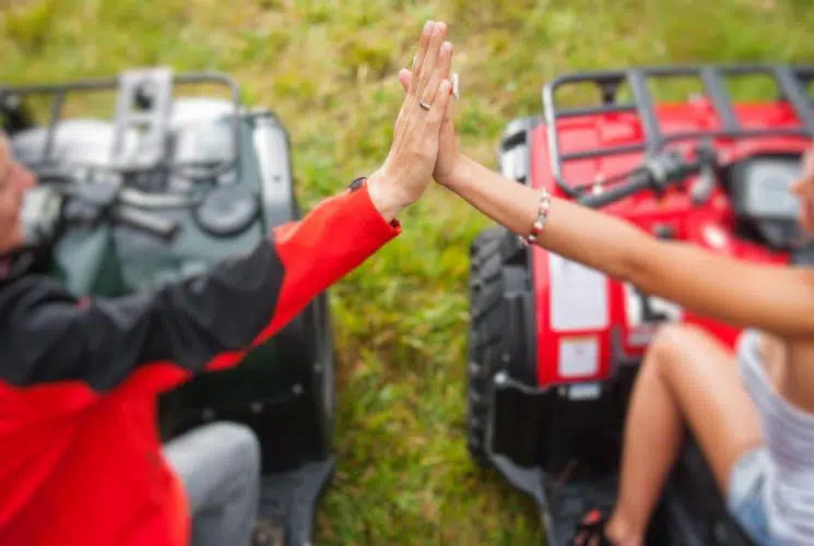Man and woman each on green and red ATVs pressing hands together