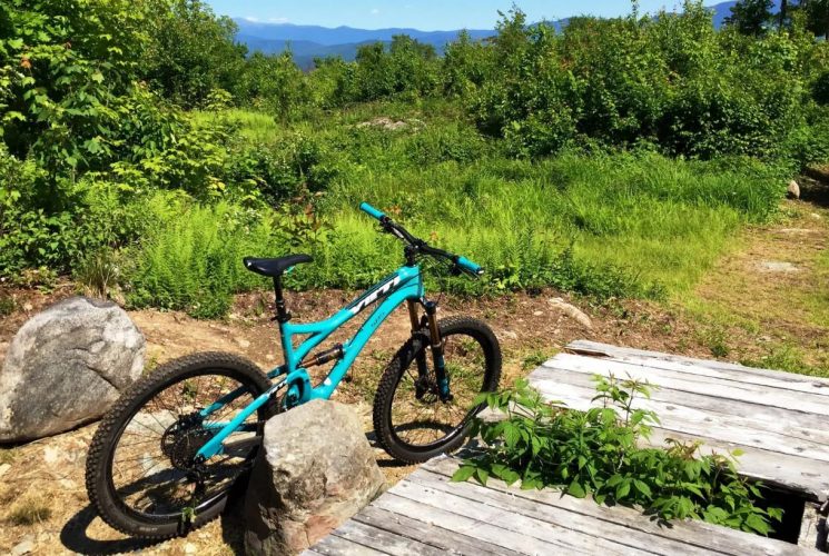Turquoise bike next to large rock and trail surrounded by green grass and trees