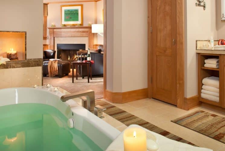Close up view of whirlpool tub full of bubbling water surrounded by lighted candles with a fireplace in the background